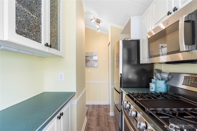 kitchen with appliances with stainless steel finishes, white cabinets, ornamental molding, and wood finished floors