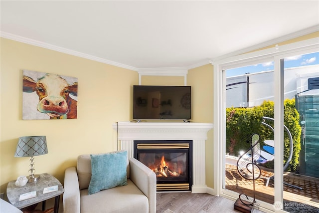 living area with a glass covered fireplace, ornamental molding, and wood finished floors