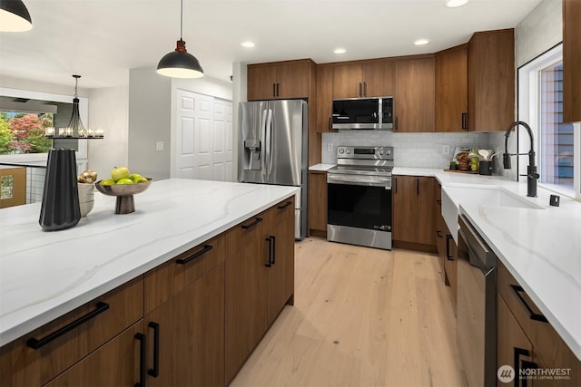 kitchen featuring a sink, stainless steel appliances, tasteful backsplash, decorative light fixtures, and light stone counters