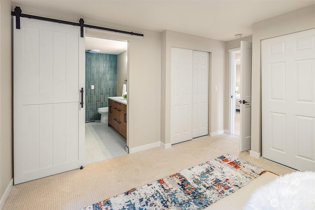 bedroom with ensuite bathroom, light carpet, a barn door, and baseboards