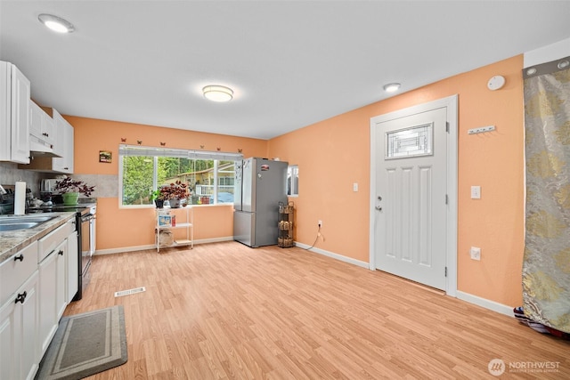 kitchen featuring a sink, white cabinets, light wood finished floors, under cabinet range hood, and stainless steel appliances