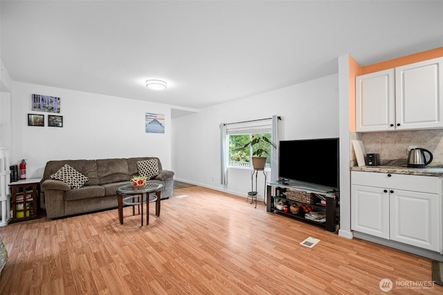 living area with baseboards, light wood-style flooring, and visible vents