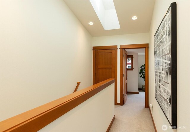 hall with baseboards, recessed lighting, light colored carpet, a skylight, and an upstairs landing
