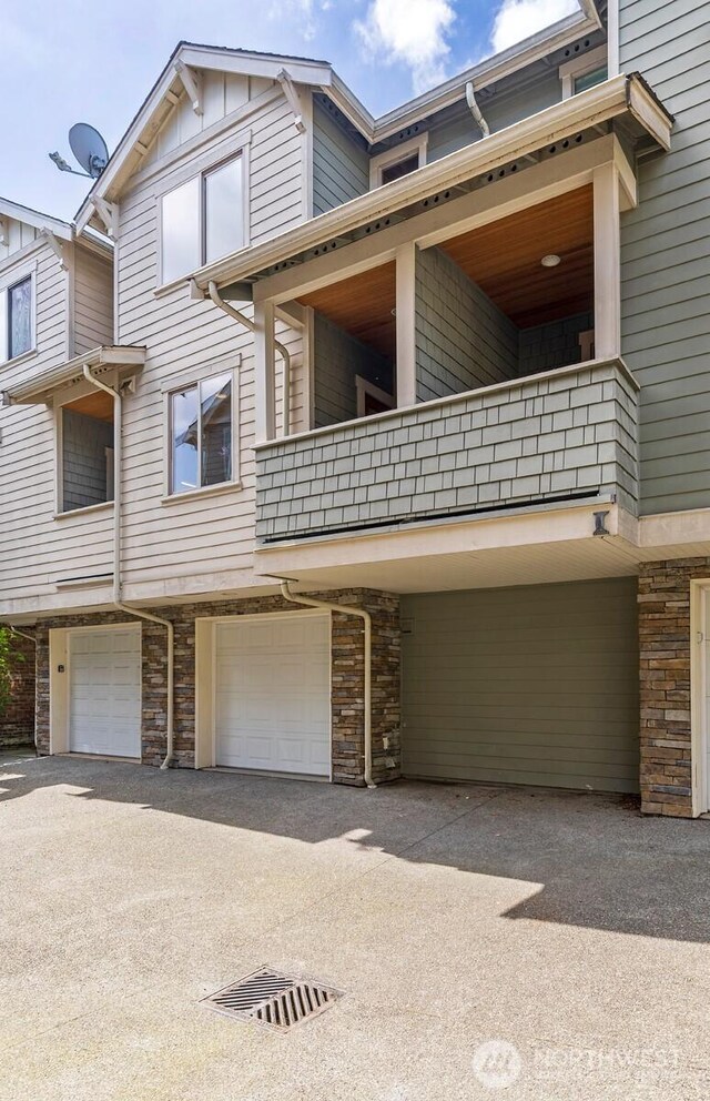 view of front facade with an attached garage, a balcony, stone siding, and aphalt driveway