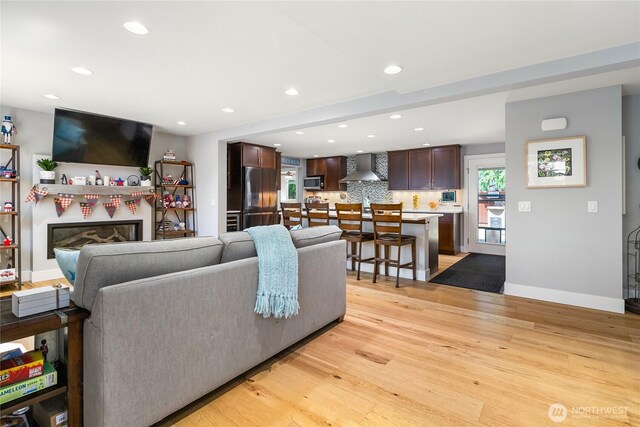 living room with recessed lighting, light wood finished floors, a glass covered fireplace, and baseboards