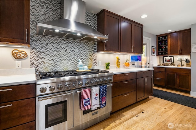 kitchen with backsplash, double oven range, light countertops, light wood-style floors, and wall chimney exhaust hood