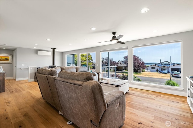 living room with ceiling fan, a wall unit AC, light wood finished floors, and a wood stove