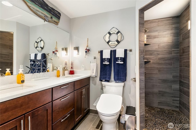 full bath with a sink, a tile shower, toilet, and double vanity