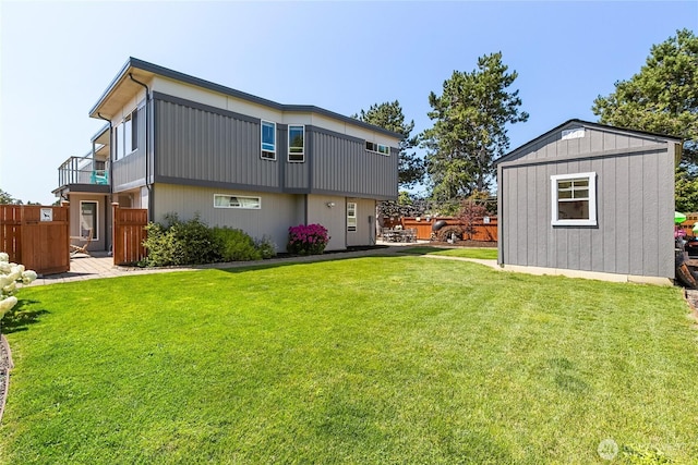 rear view of house featuring a lawn, an outbuilding, fence, and a balcony