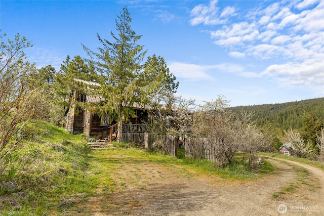 view of street featuring stairway, a forest view, and dirt driveway