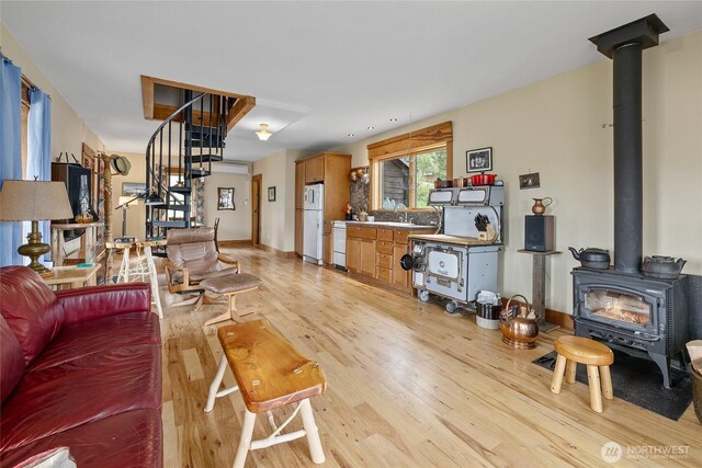 living room featuring baseboards, a wood stove, light wood-style flooring, and stairs