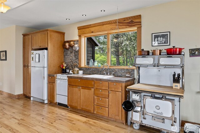kitchen with white appliances, backsplash, a sink, and light wood-style floors
