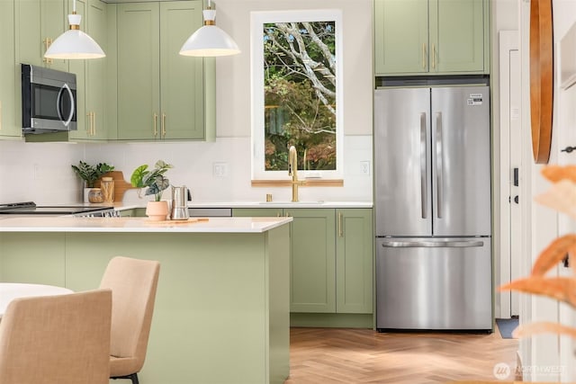 kitchen with backsplash, appliances with stainless steel finishes, a sink, light countertops, and green cabinetry