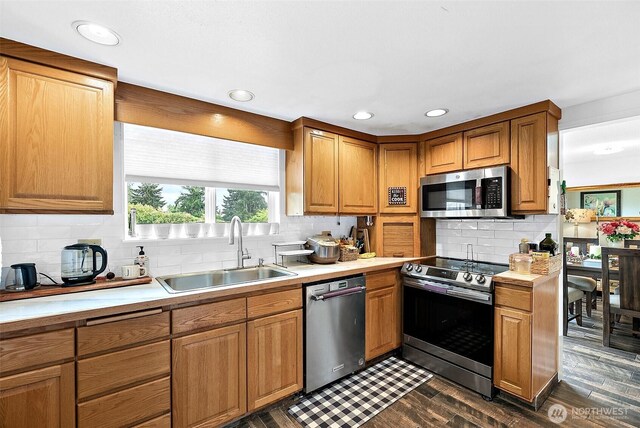kitchen with appliances with stainless steel finishes, a sink, light countertops, tasteful backsplash, and dark wood-style floors