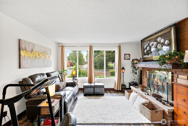 living room featuring a brick fireplace, a textured ceiling, and wood finished floors