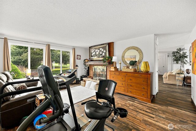 exercise room with a textured ceiling, dark wood-style flooring, and a fireplace