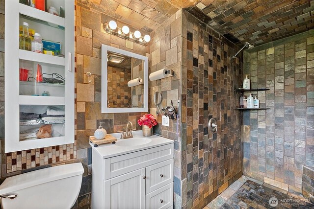bathroom featuring vanity, a tile shower, toilet, and tile walls
