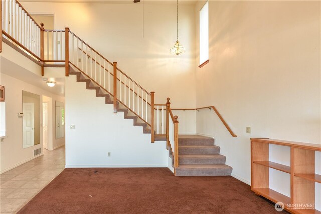 stairway featuring a towering ceiling, carpet, and baseboards