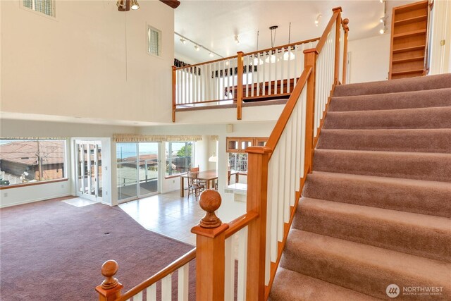 stairs with a towering ceiling, track lighting, a ceiling fan, carpet floors, and french doors