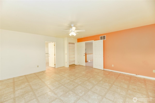 unfurnished bedroom with baseboards, a walk in closet, tile patterned floors, ensuite bathroom, and a ceiling fan