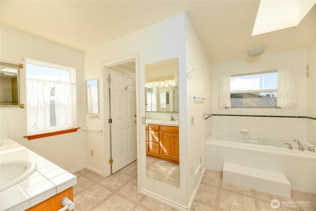 full bathroom featuring vanity, a garden tub, a skylight, baseboards, and tile patterned floors