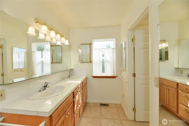 bathroom featuring healthy amount of natural light, baseboards, double vanity, and backsplash