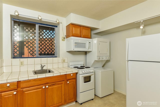 kitchen with white appliances, a sink, stacked washing machine and dryer, tile countertops, and decorative backsplash