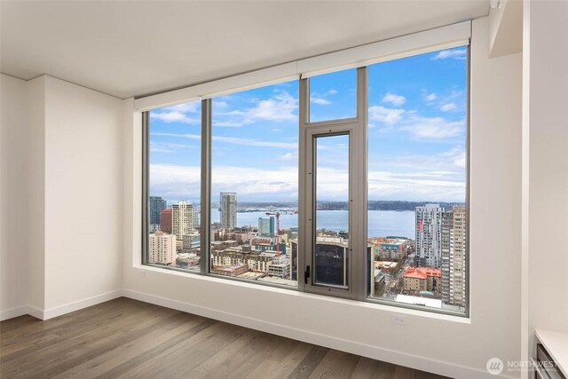 empty room featuring baseboards, dark wood-type flooring, a water view, and a view of city