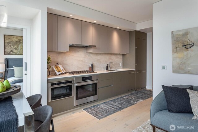 kitchen with light wood-style floors, stainless steel appliances, decorative backsplash, gray cabinetry, and modern cabinets