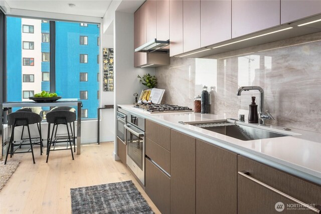 kitchen featuring light countertops, a sink, light wood finished floors, and tasteful backsplash