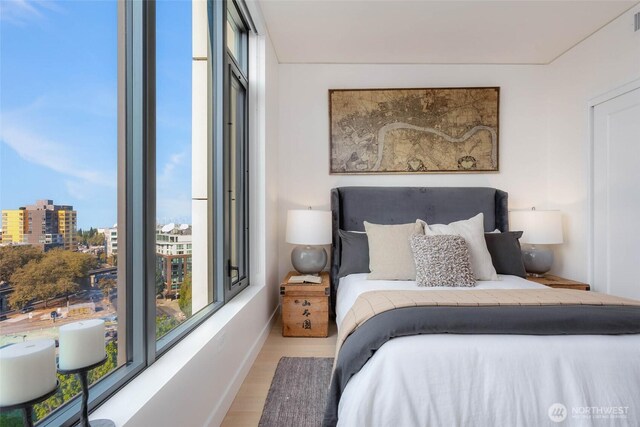 bedroom with baseboards, multiple windows, a city view, and wood finished floors