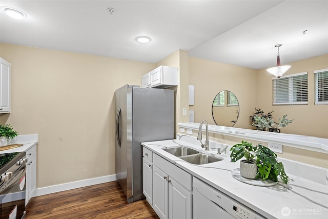 kitchen with appliances with stainless steel finishes, a sink, light countertops, dark wood finished floors, and baseboards