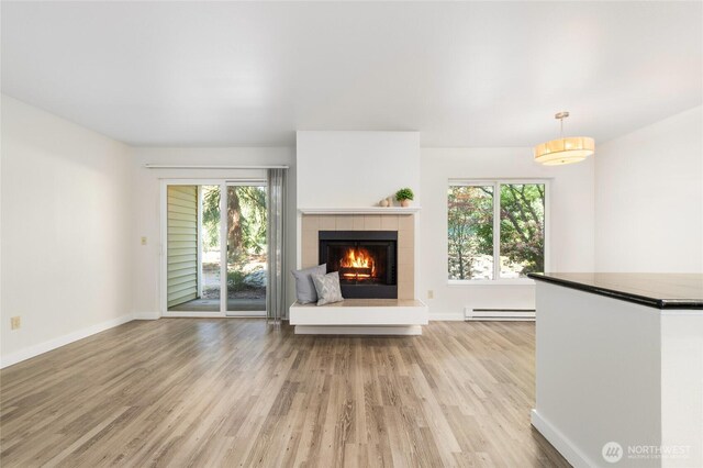 unfurnished living room with baseboards, a tile fireplace, baseboard heating, and light wood-type flooring