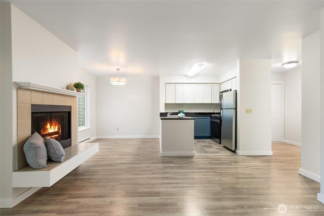 kitchen featuring freestanding refrigerator, dark countertops, open floor plan, stove, and light wood-style flooring