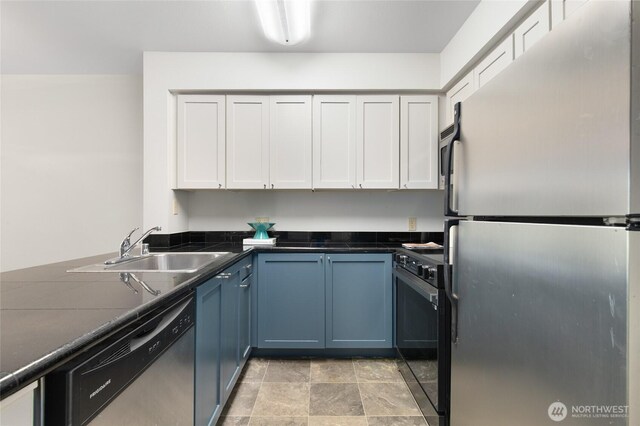 kitchen with dark countertops, appliances with stainless steel finishes, a sink, white cabinetry, and stone finish flooring