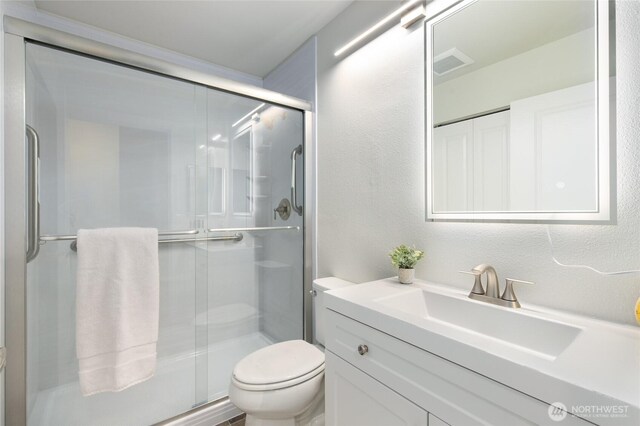 bathroom with vanity, a shower stall, toilet, and visible vents