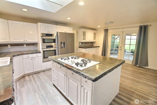 kitchen with a skylight, light wood-style floors, stainless steel appliances, recessed lighting, and white cabinetry
