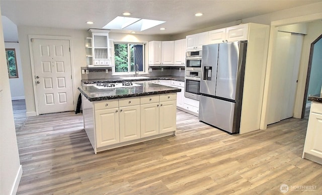 kitchen with a skylight, appliances with stainless steel finishes, open shelves, light wood-type flooring, and white cabinets