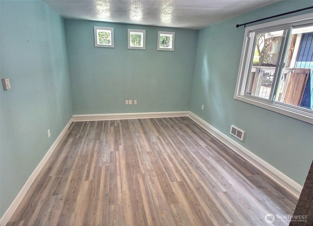unfurnished room featuring visible vents, baseboards, wood finished floors, and a wealth of natural light