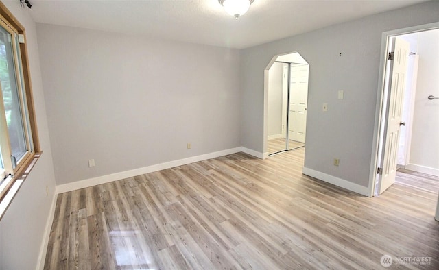 unfurnished room with light wood-style floors, arched walkways, and baseboards