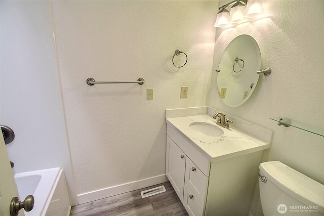 bathroom featuring visible vents, wood finished floors, vanity, baseboards, and toilet