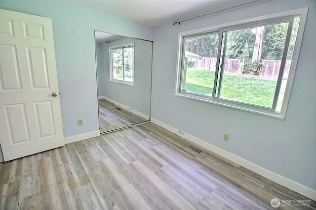 unfurnished bedroom featuring baseboards, a closet, wood finished floors, and visible vents