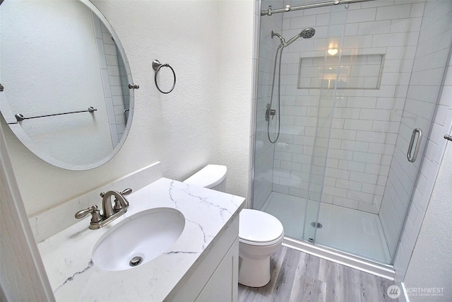 bathroom with vanity, wood finished floors, toilet, and a shower stall