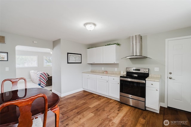 kitchen with wall chimney range hood, electric range, white cabinets, light wood finished floors, and light countertops