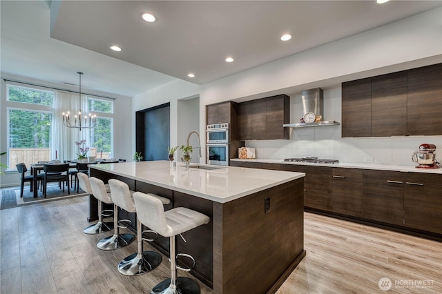 kitchen with appliances with stainless steel finishes, modern cabinets, a sink, a breakfast bar, and wall chimney exhaust hood