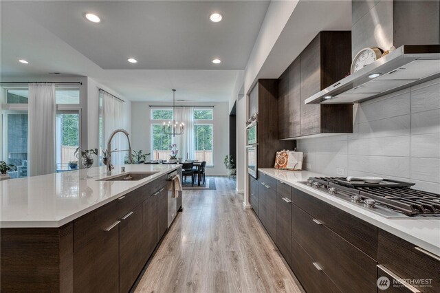 kitchen featuring wall chimney range hood, appliances with stainless steel finishes, modern cabinets, light wood-type flooring, and a sink