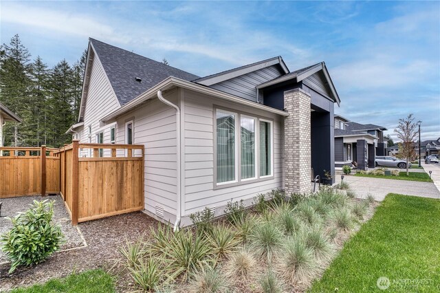 view of side of home with fence and a shingled roof