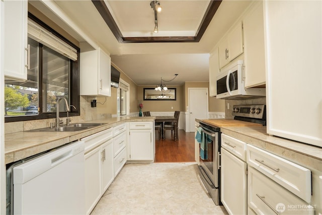 kitchen with track lighting, white appliances, light countertops, a raised ceiling, and a sink