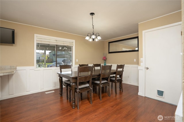 dining area with wood finished floors, an inviting chandelier, a wainscoted wall, and a decorative wall