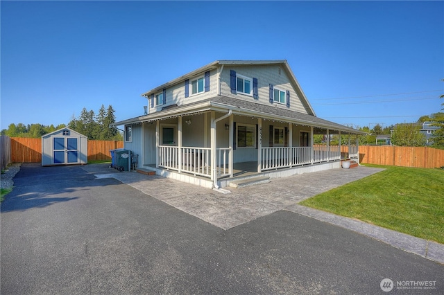 farmhouse featuring covered porch, fence, a storage shed, and a front lawn